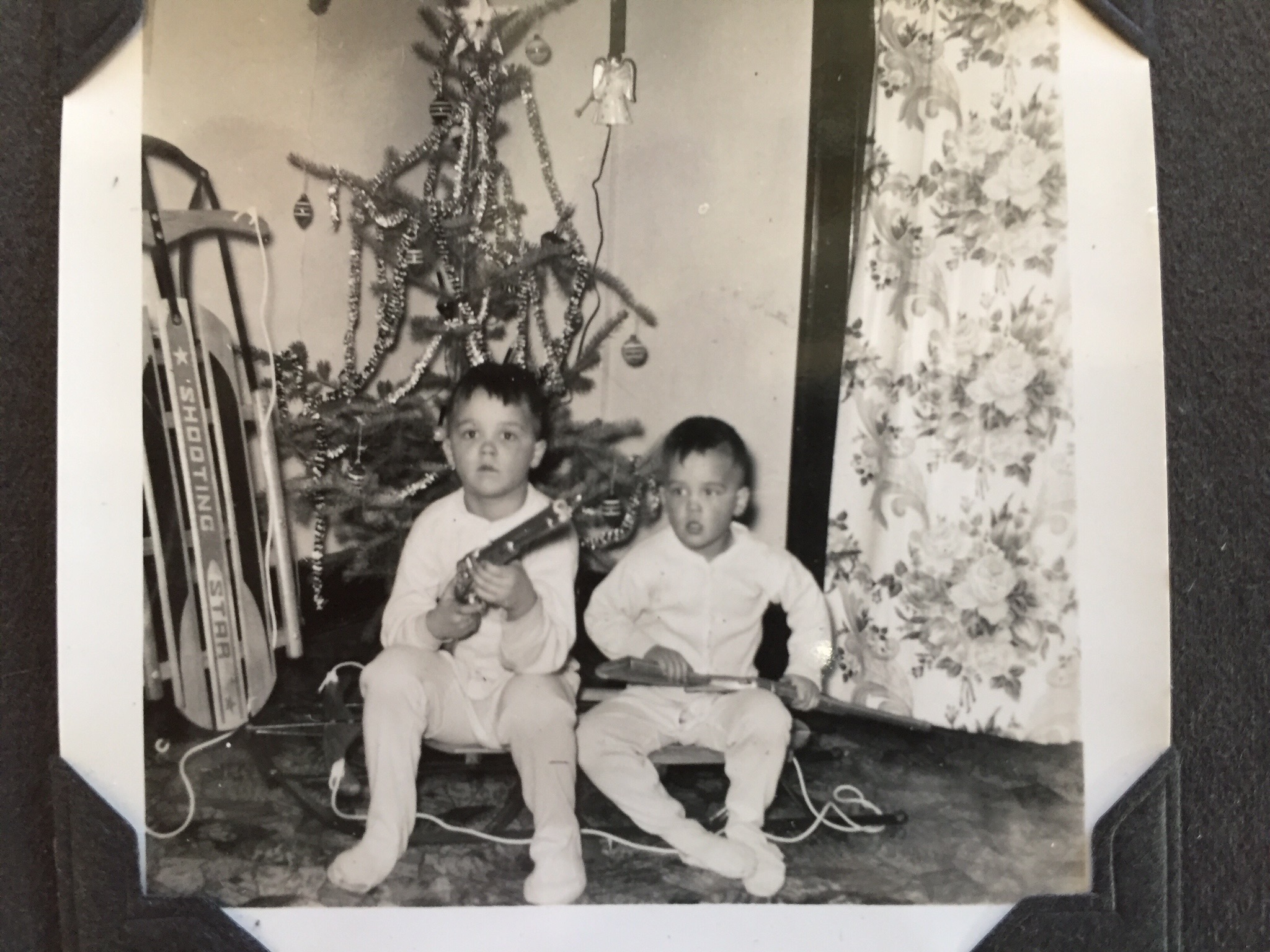Mac and his younger brother Darrel beside a Christmas tree and sleds.