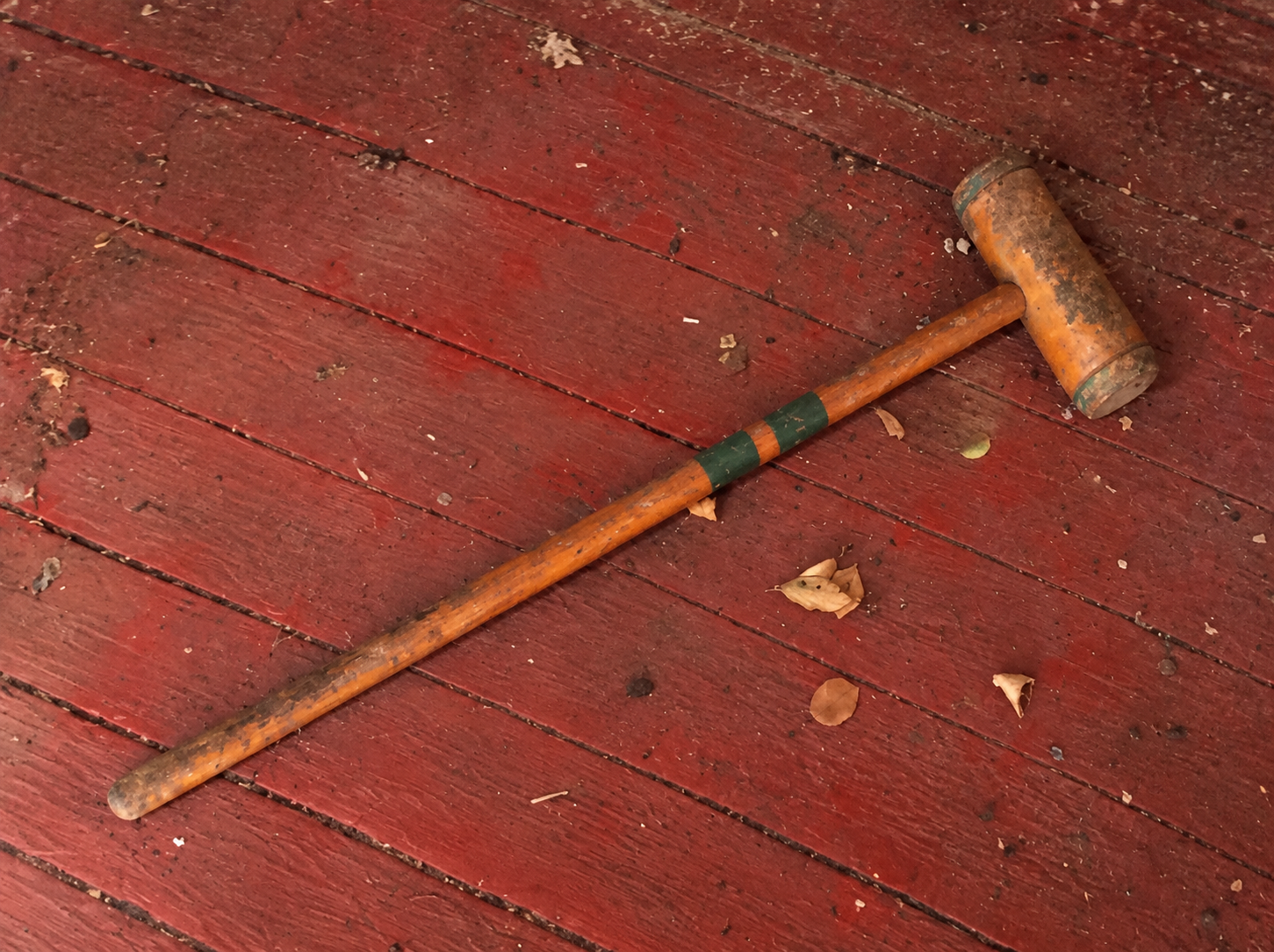 Mac’s childhood wooden croquet mallet, with green bands on its handle, lying on worn red floorboards.